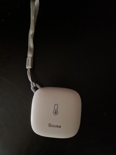Ein weißes Govee-Thermometer mit einem Thermometersymbol und dem Govee-Logo, das an einer Schnur hängt.
