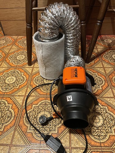 Ein Lüfter mit einem flexiblen Schlauch und einem Vorfilter, der auf einem gemusterten Boden steht.