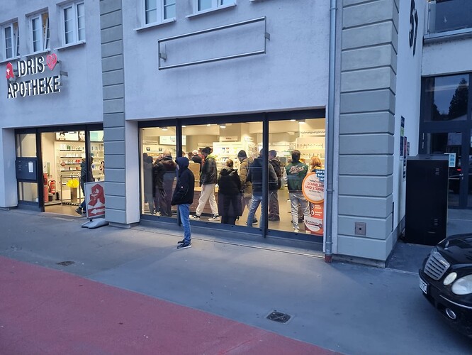 Eine Apotheke mit dem Namen "Idris Apotheke" und einer Schlange von Kunden, die drinnen stehen.