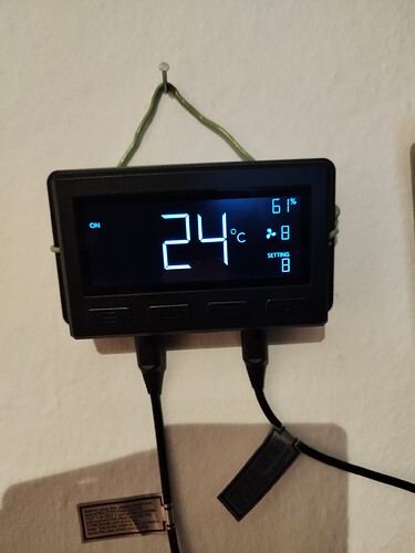 Ein digitales Klimakontrollgerät mit einem blauen Display, das die Temperatur auf 24°C und die Luftfeuchtigkeit auf 61% anzeigt. Es sind zwei Kabel angeschlossen.