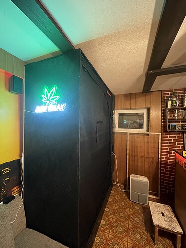 Ein schwarzer Grow-Schrank mit einer grünen Neonreklame, auf der ein Cannabisblatt und die Worte "JUST RELAX" abgebildet sind.