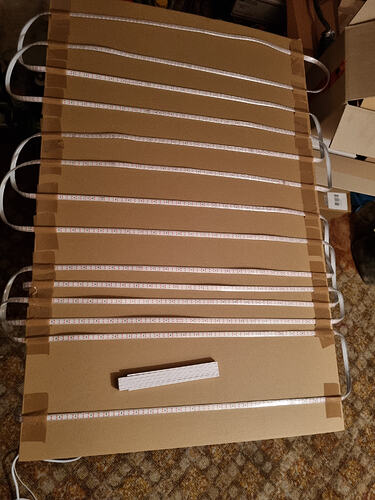 Ein großes Stück Pappe, das mit mehreren Reihen von LED-Streifen bedeckt ist, die mit Klebeband befestigt sind.