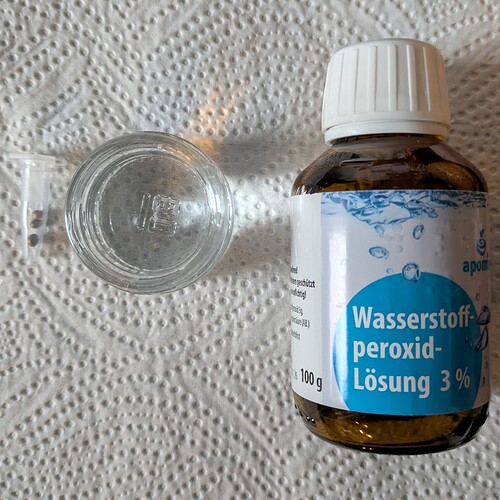 Cannabissamen in einem kleinen Röhrchen neben einem Glas und einer Flasche Wasserstoffperoxid-Lösung zur Keimung.