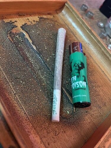 Ein Joint liegt neben einem grünen Feuerzeug auf einem Holztablett. Das Feuerzeug hat die Aufschrift "GREEN POISON" und "sweetseeds.com".