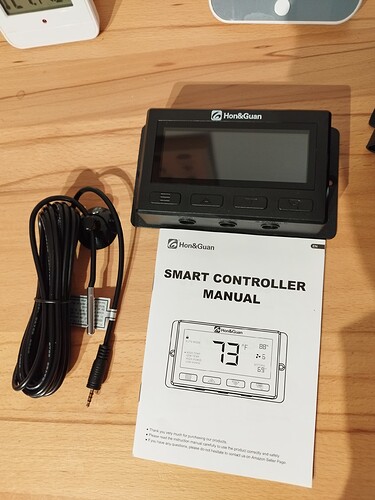 Ein digitaler Smart Controller von Hon&Guan mit einem dazugehörigen Handbuch liegt auf einem Holztisch.