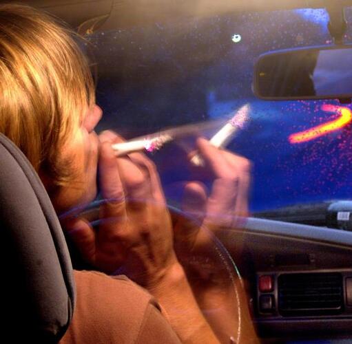 Ein Autofahrer hÀlt hinter dem Steuer eines Autos einen Joint in der Hand.