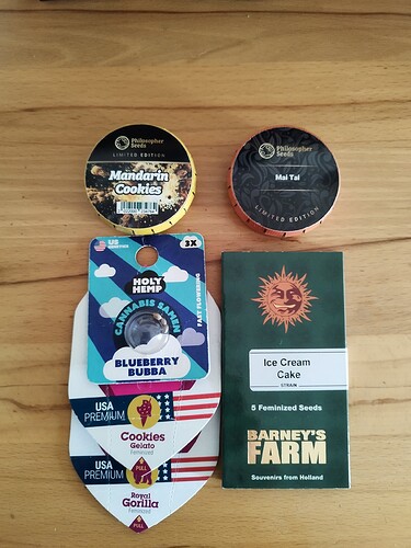 Mehrere Packungen mit Cannabissamen und eine Packung mit Eiscreme-Kuchen-Samen von Barney's Farm liegen auf einem Holztisch.