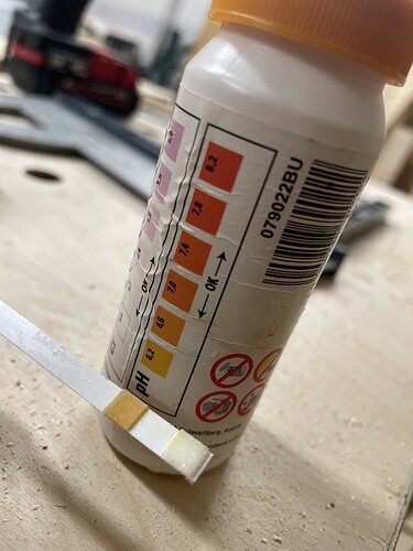 Ein pH-Teststreifen wird neben einer Flasche mit pH-Teststäbchen gehalten, die verschiedene Farbbereiche für den pH-Wert anzeigen.