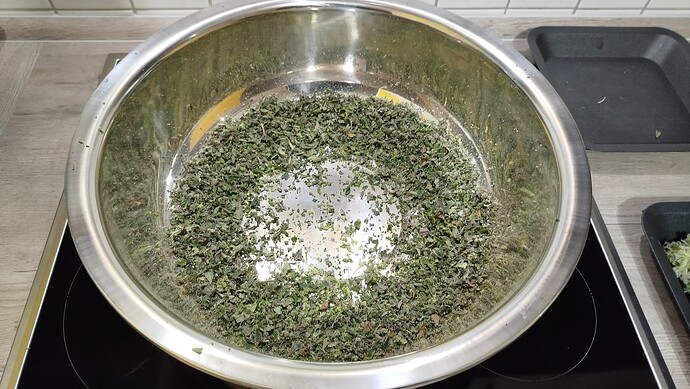 Eine Edelstahlschüssel gefüllt mit zerkleinertem Cannabis-Verschnitt auf einem Herd.