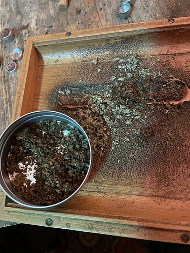 Ein Holzteller mit zerkleinertem Cannabis und einem Metallbehälter voller Cannabisblüten.