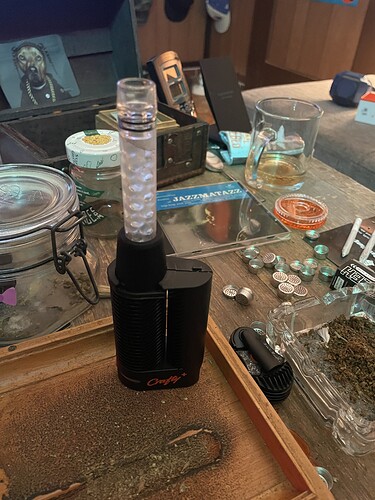Ein schwarzer Vaporizer namens Crafty+ steht auf einem Holztisch, daneben liegen Cannabis-Blüten und Zubehör.