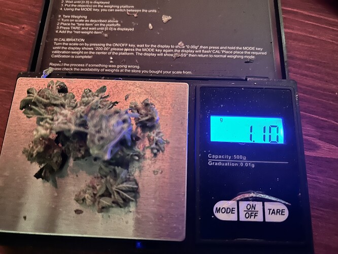 Eine digitale Waage zeigt 1,10 Gramm an, daneben liegen getrocknete Cannabis-Buds.