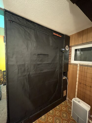 Eine geschlossene schwarze Growbox mit dem Logo "Spider Farmer" oben rechts. Daneben befindet sich ein Fenster und ein Luftentfeuchter.