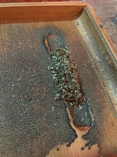 Ein Haufen zerkleinerter Cannabisknospen liegt auf einem hölzernen Tablett, das mit Cannabisresten bedeckt ist.