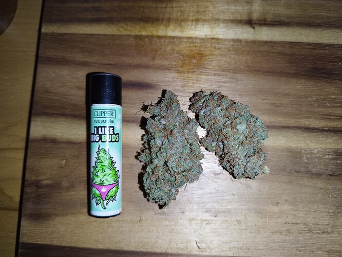 Zwei getrocknete Cannabis-Buds liegen neben einem Feuerzeug mit der Aufschrift "I LIKE BIG BUDS".