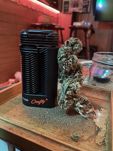 Ein getrockneter Cannabis-Bud liegt neben einem schwarzen Vaporizer auf einem Holztablett.