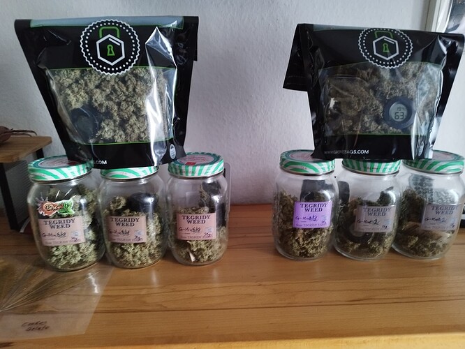 Mehrere Gläser und Beutel gefüllt mit getrockneten Cannabisblüten, beschriftet mit 'G-Mint'.