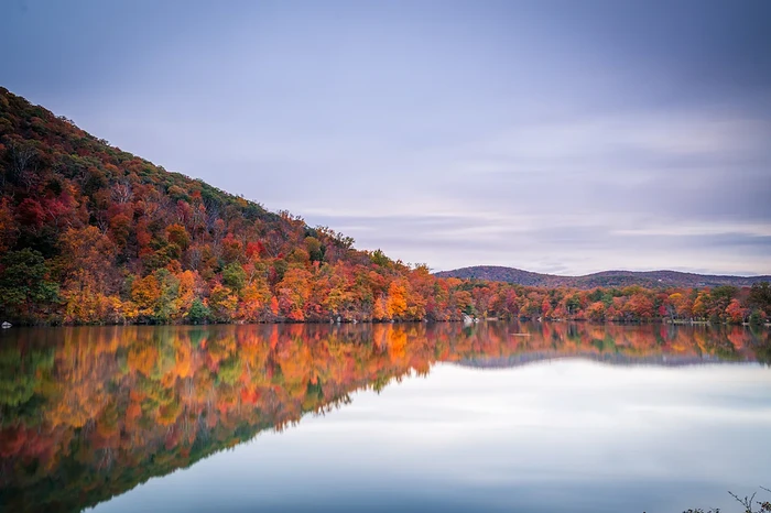 The Amtrak Adirondack Line passes Lake Champlain, offering sweeping views of fall foliage mirrored in the water